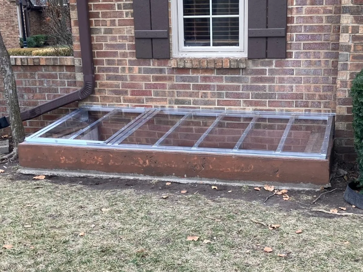 Window well cover on dark brick home with gravel surround