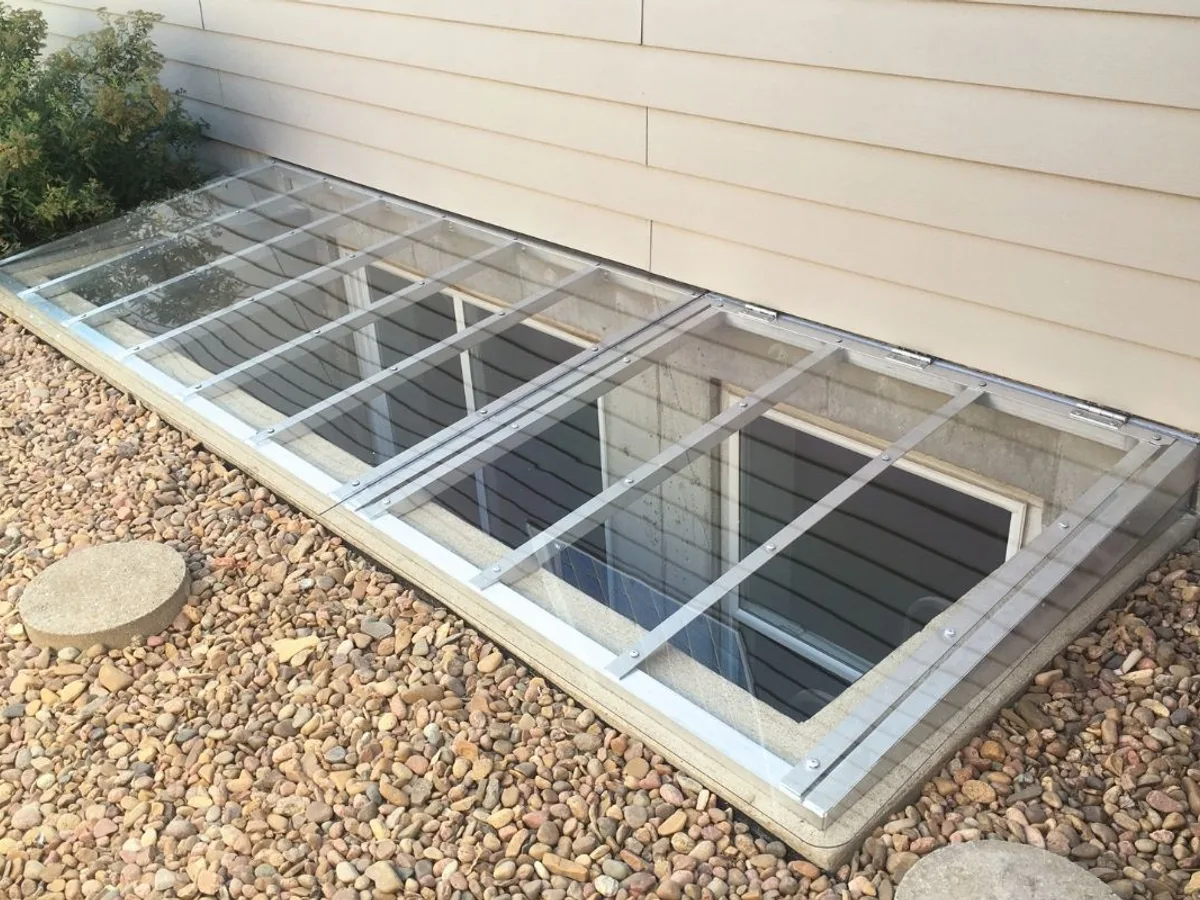 Window well cover closed on gravel surround showing aluminum frame and clear polycarbonate