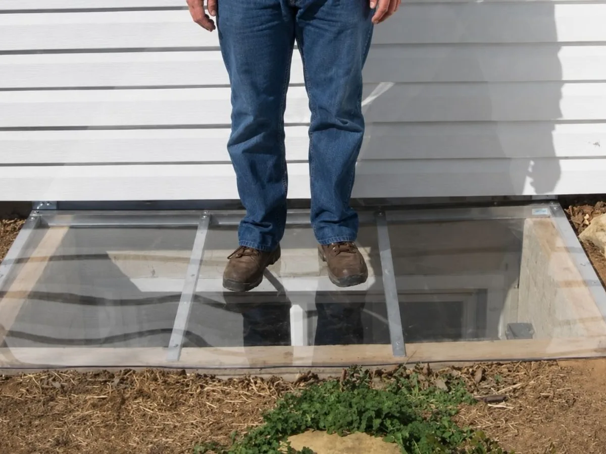 Adult standing on a window well cover to demonstrate its strength